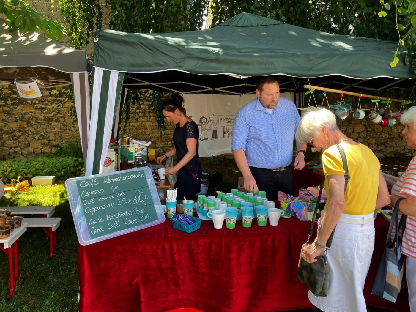 Stand des Fördervereins mit Tafel „Café Lemmchenschule“, Kaffeebechern und Basteleien, Gäste beim Einkaufen